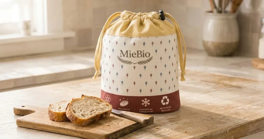 Sac à pain MieBio fermé sur un pain, tranches encore moelleuses sur une planche