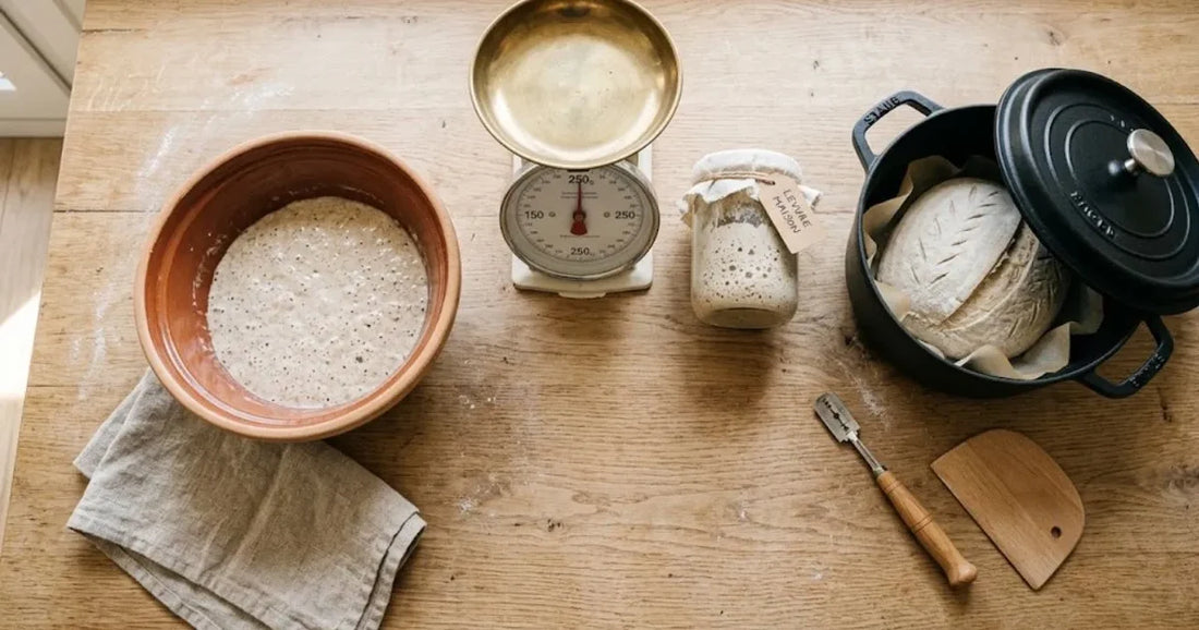 Bocal de levain, balance, saladier, cocotte, lame et coupe-pâte posés à plat